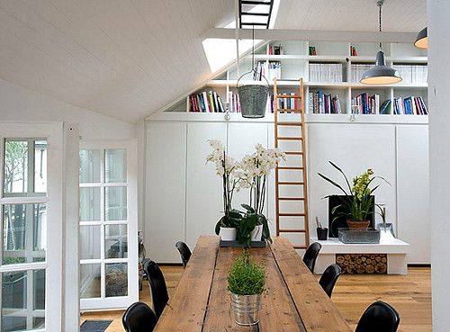 a wooden table with chairs and plants on it in a room that has white walls