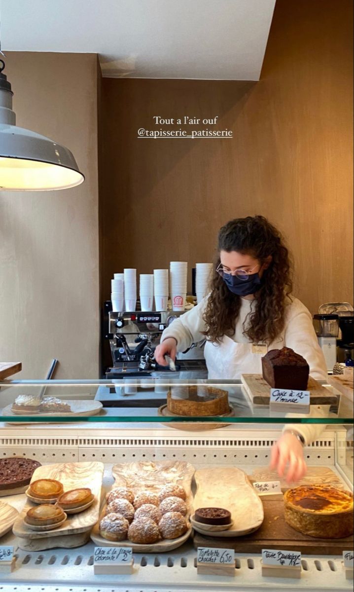 a woman wearing a face mask behind a counter filled with pastries