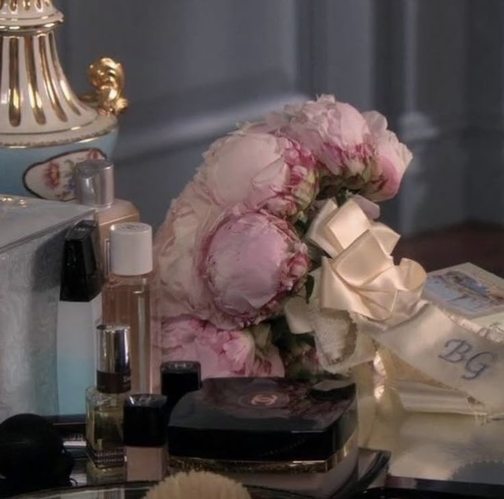 a bouquet of pink flowers sitting on top of a table next to cosmetics and perfume bottles