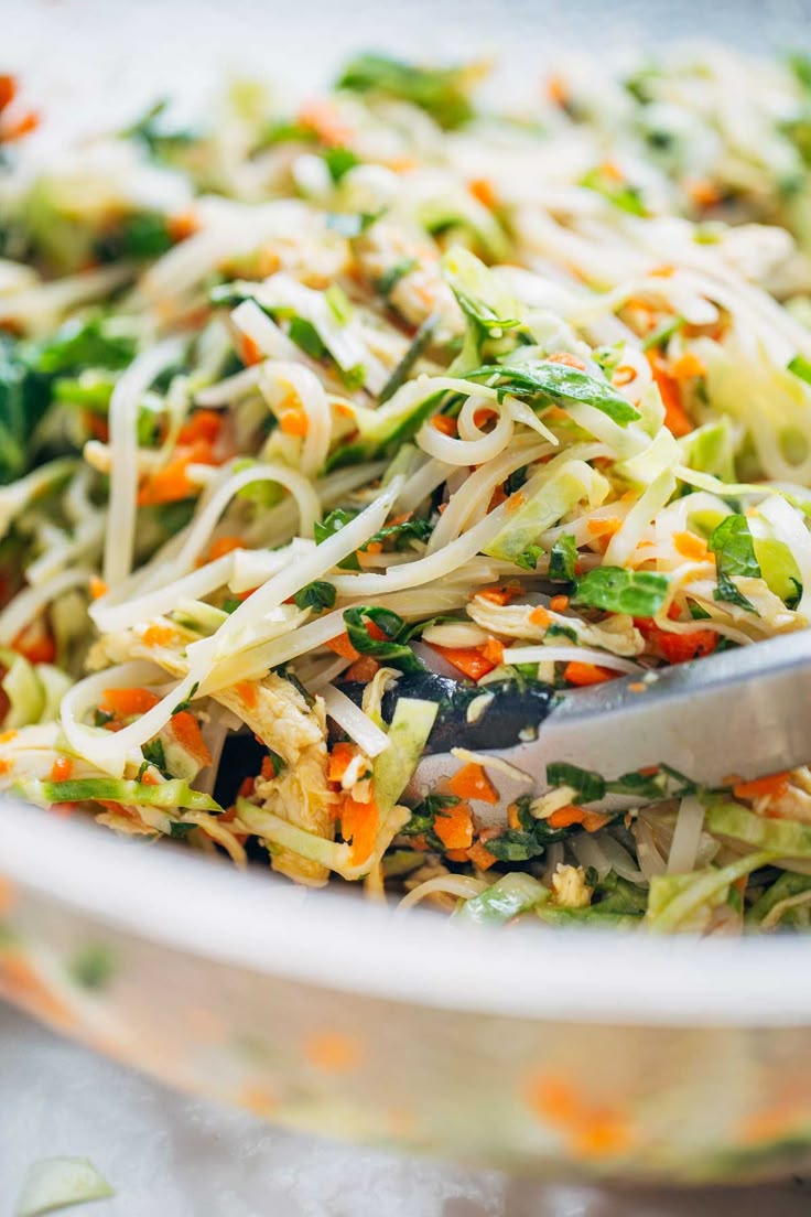 a salad with carrots, broccoli and sprouts in a white bowl