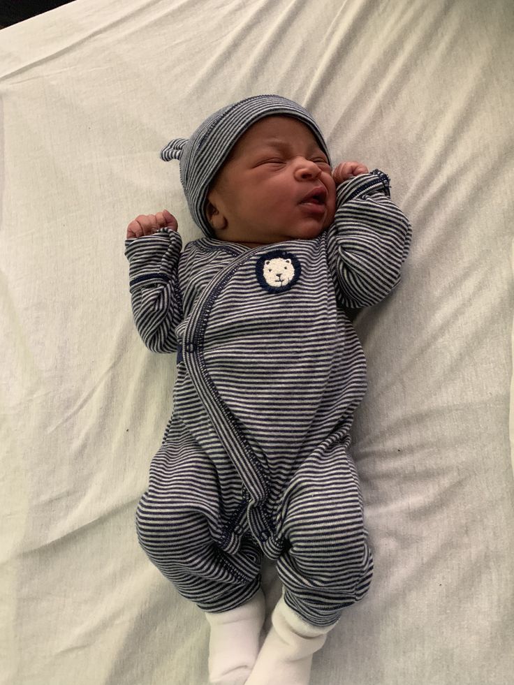 a baby laying on top of a bed wearing a blue and white striped suit with buttons