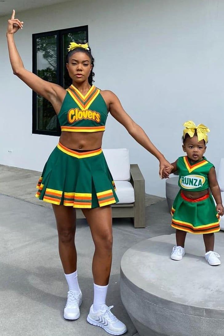 a woman in a green cheerleader outfit holding hands with a child wearing white tennis shoes