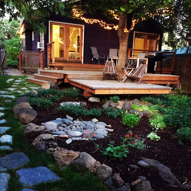 a small backyard with rocks and grass around the patio area, along with steps leading to an outdoor deck