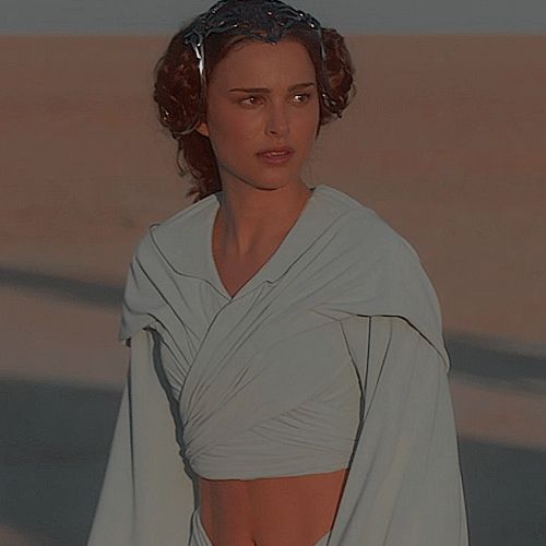 a woman in a white dress and headpiece walking on the beach with her hair pulled back