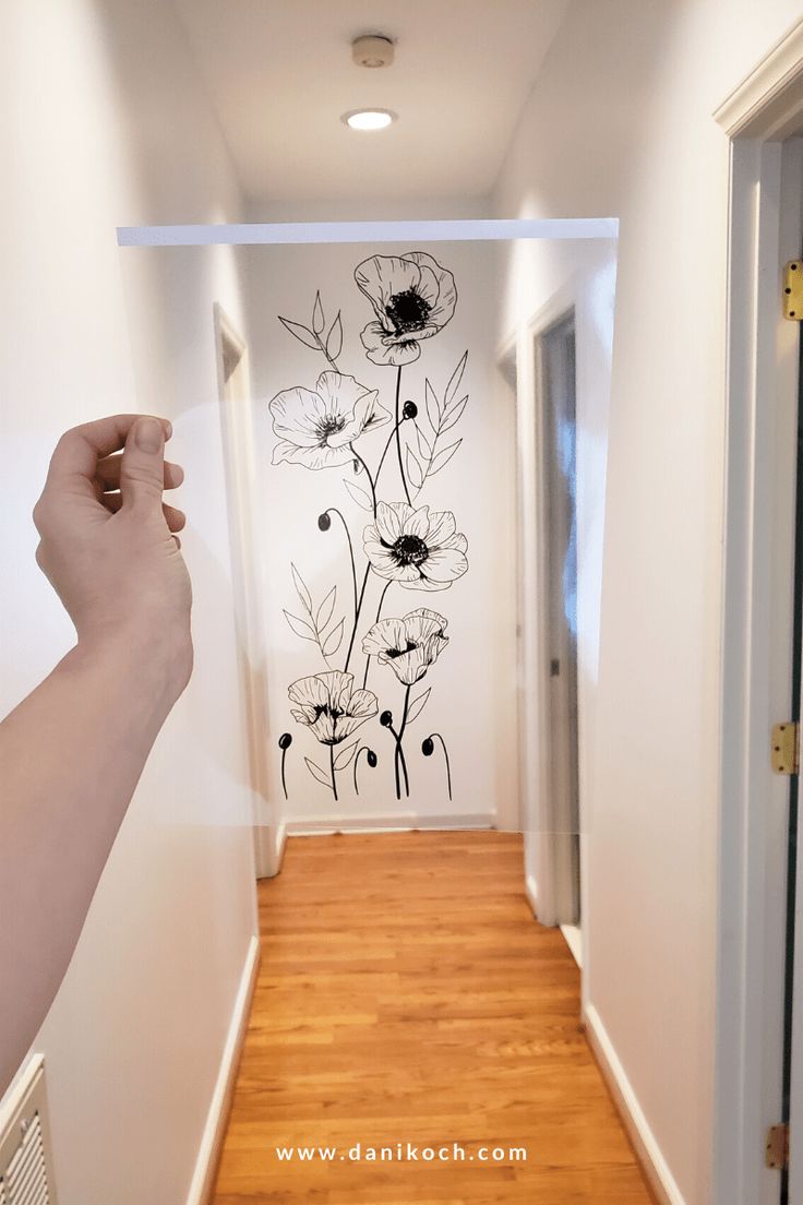 a hand is holding up a wall decal in the middle of an empty hallway