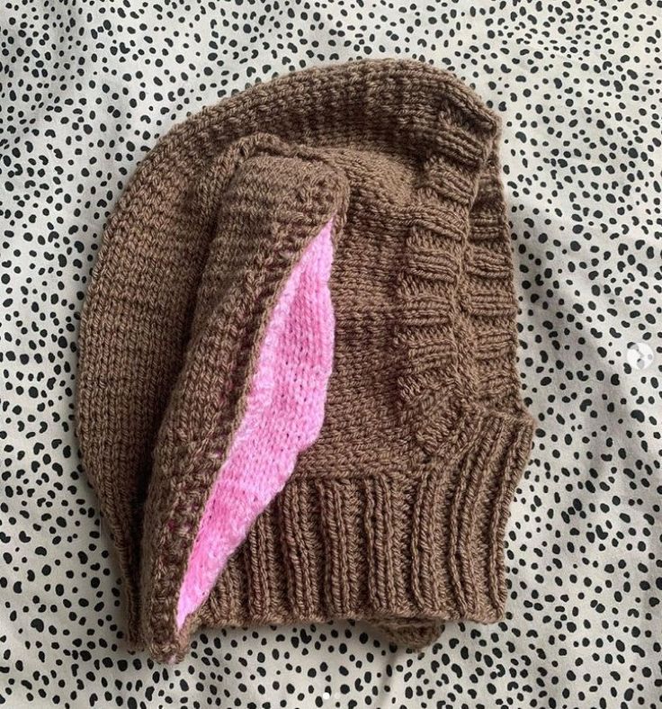 a knitted hat with a pink ear laying on top of a polka dot blanket