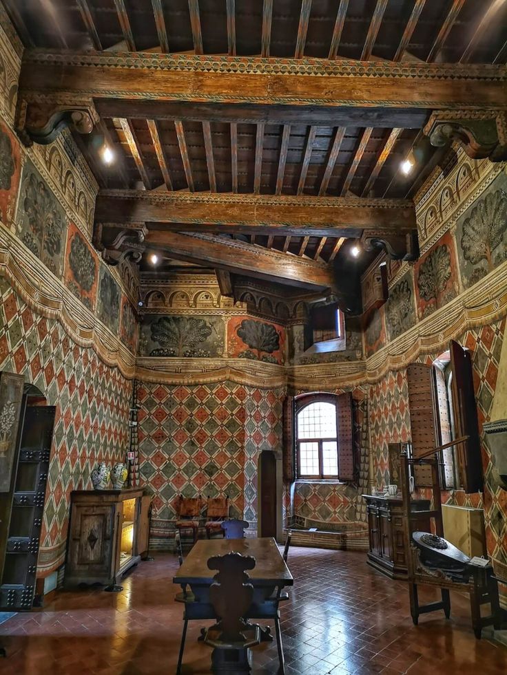 an ornately decorated room with high ceilings and wooden tables in the foreground is a fireplace