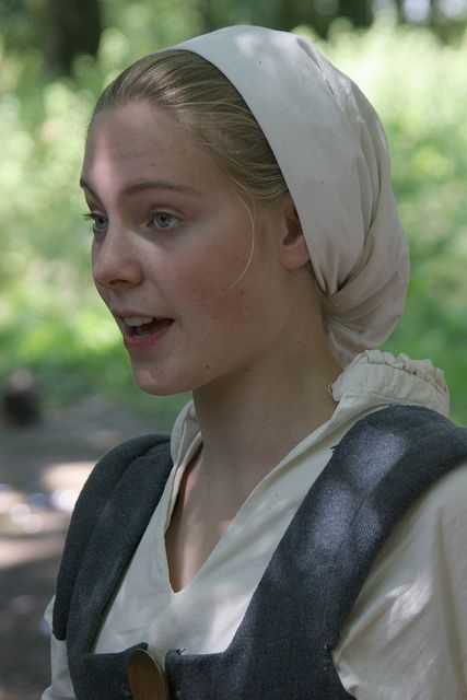 a woman with a white head scarf is standing in the woods and looking off to the side