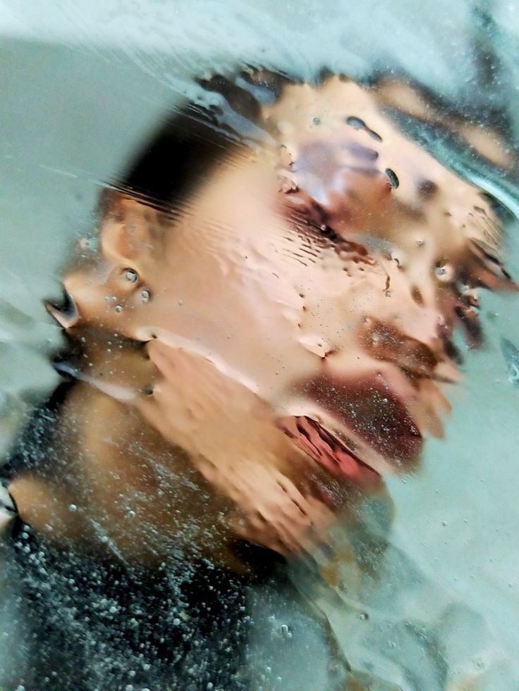 a woman's face is reflected in the water with drops of water on it