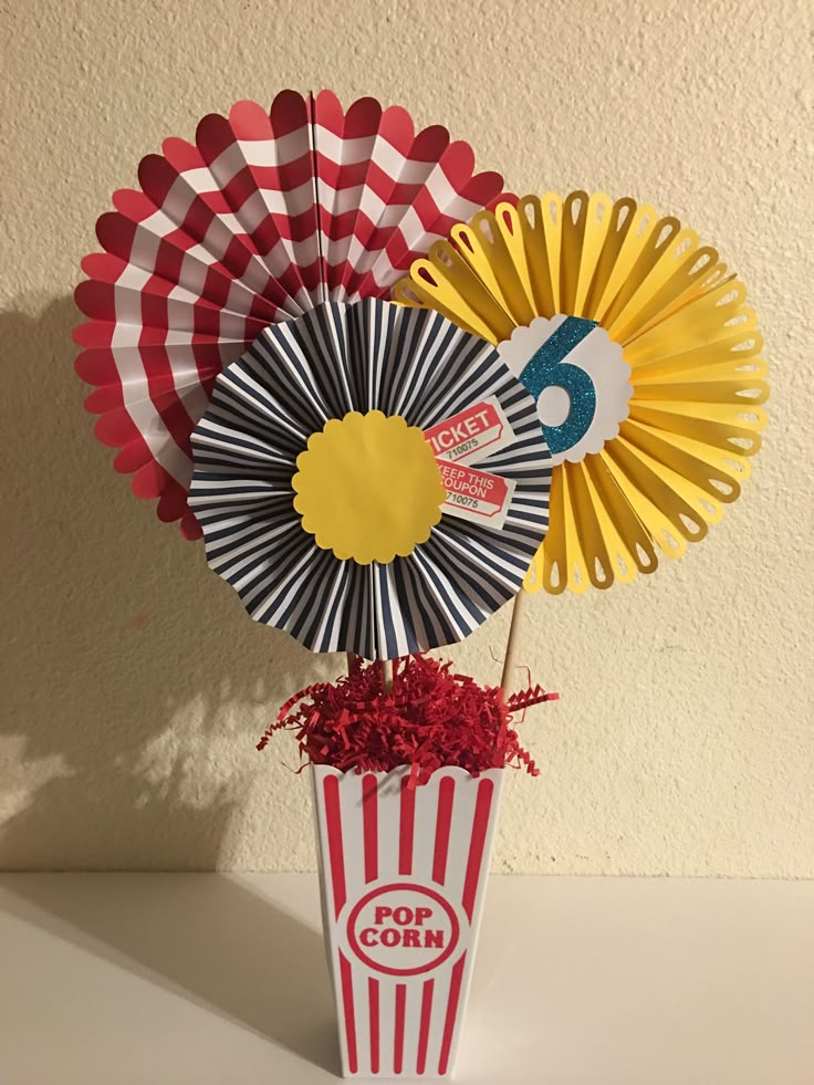 some paper fans are in a vase with red and yellow flowers on it, along with other decorations