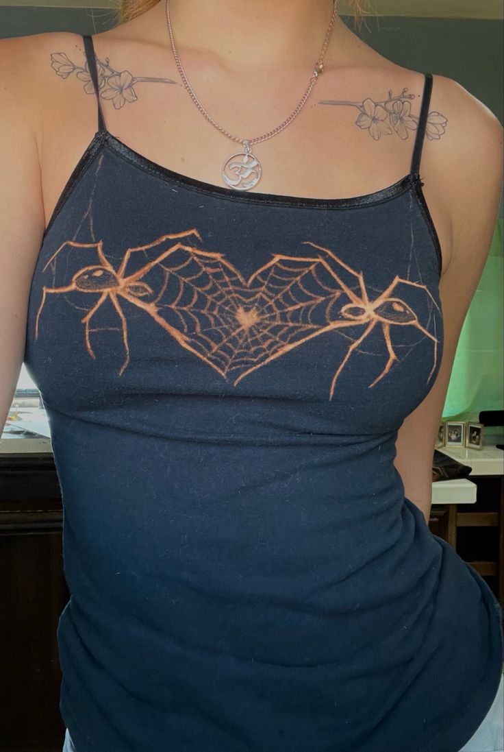 a woman wearing a blue tank top with an orange spider web heart on it's chest