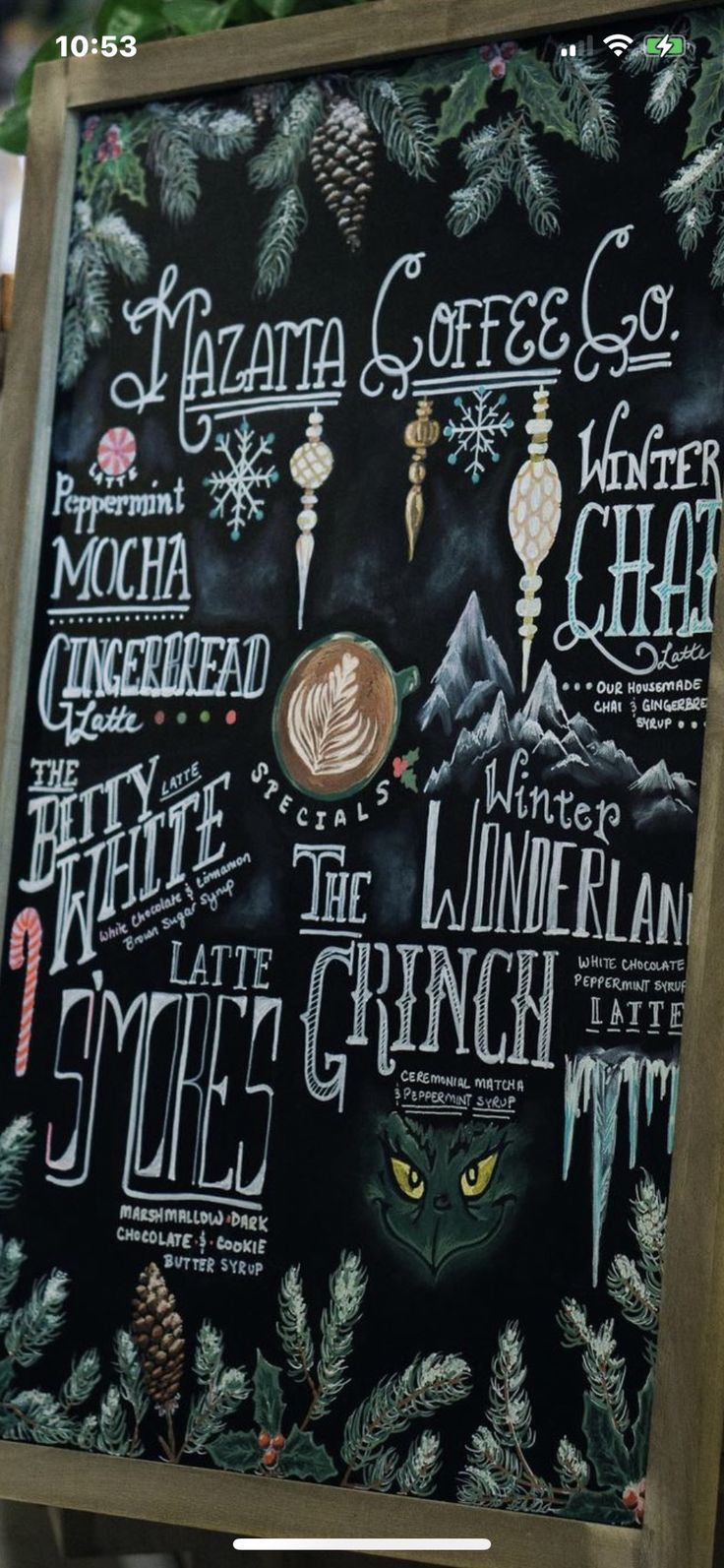 a chalkboard sign with the names of coffee and other things on it in front of a christmas tree