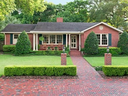 a red brick house surrounded by green bushes and trimmed with boxwood trees in the front yard