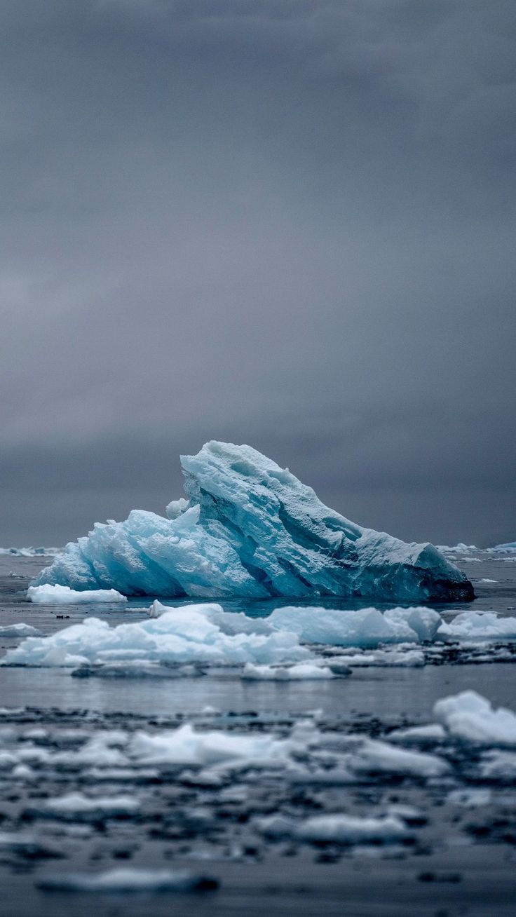 an iceberg floating in the ocean on a cloudy day