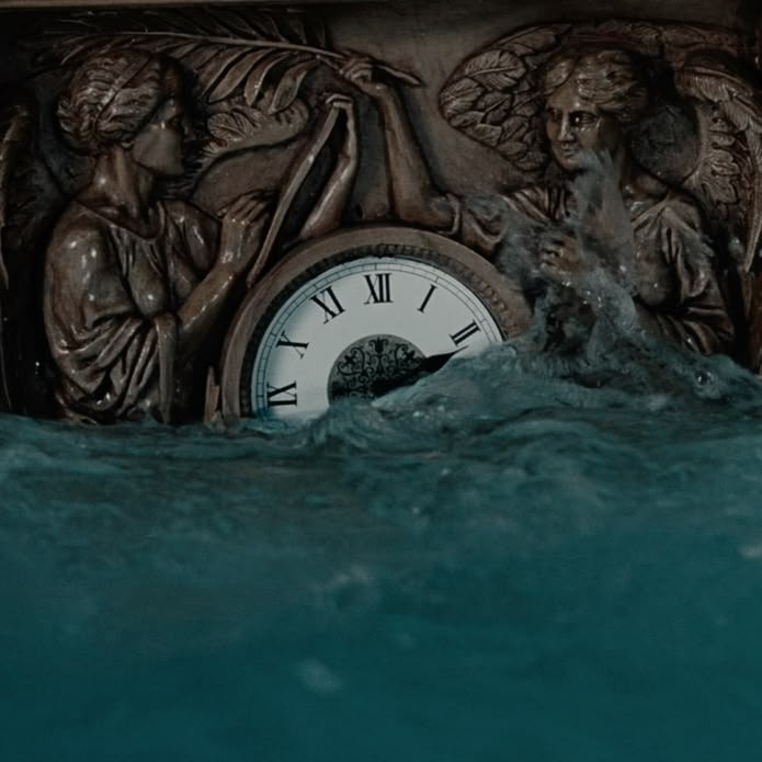 a clock in the middle of water with angels on it's sides and an angel statue next to it