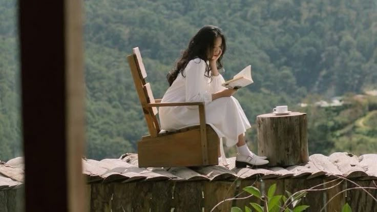 a woman sitting on top of a wooden chair next to a tree stump reading a book