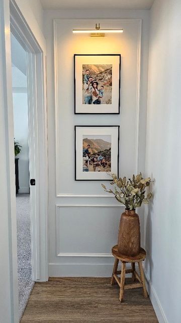 an empty hallway with pictures on the wall and a wooden stool in front of it