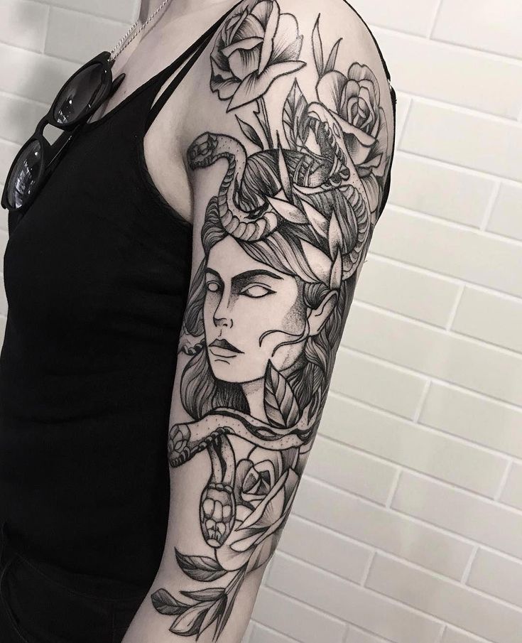 a woman's arm with flowers and leaves tattooed on her shoulder, in front of a white brick wall