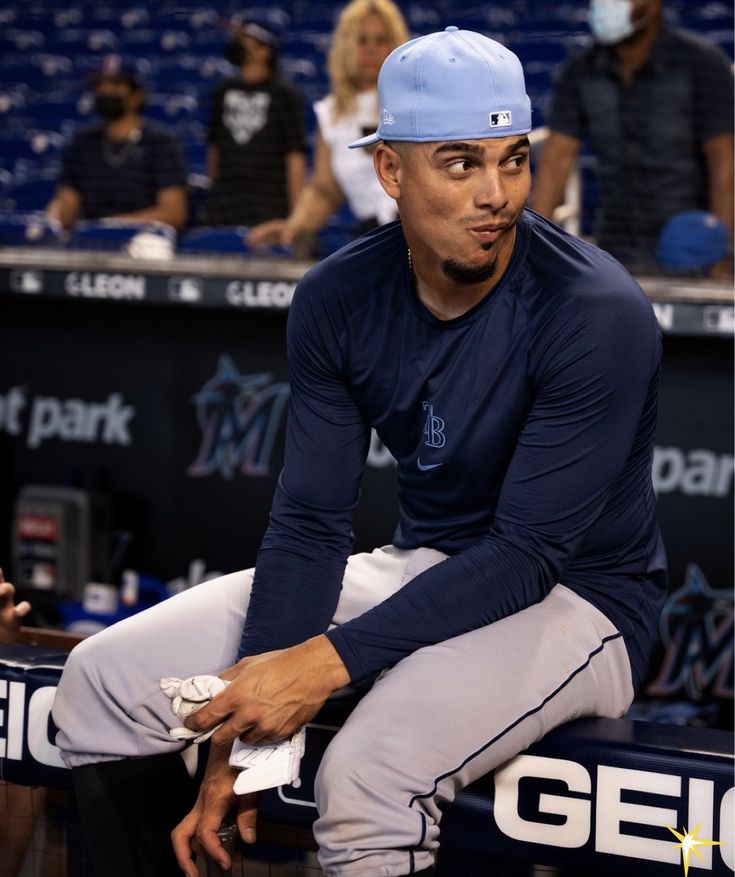 a baseball player sitting on the bench in front of an audience wearing a blue hat