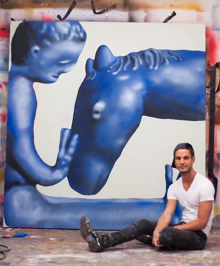 a man sitting on the ground in front of a large blue horse painting with his legs crossed