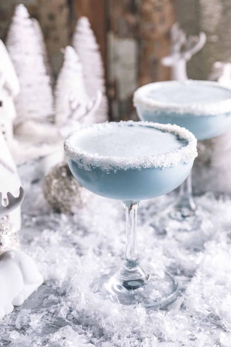 two blue margaritas sitting on top of snow covered ground next to christmas trees and decorations