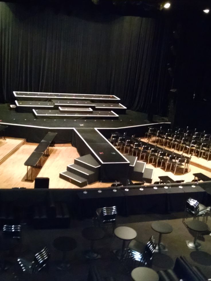 an empty stage with chairs and stools in the center, surrounded by black curtains