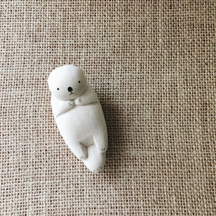 a small white teddy bear laying on top of a brown cloth covered floor next to a wall