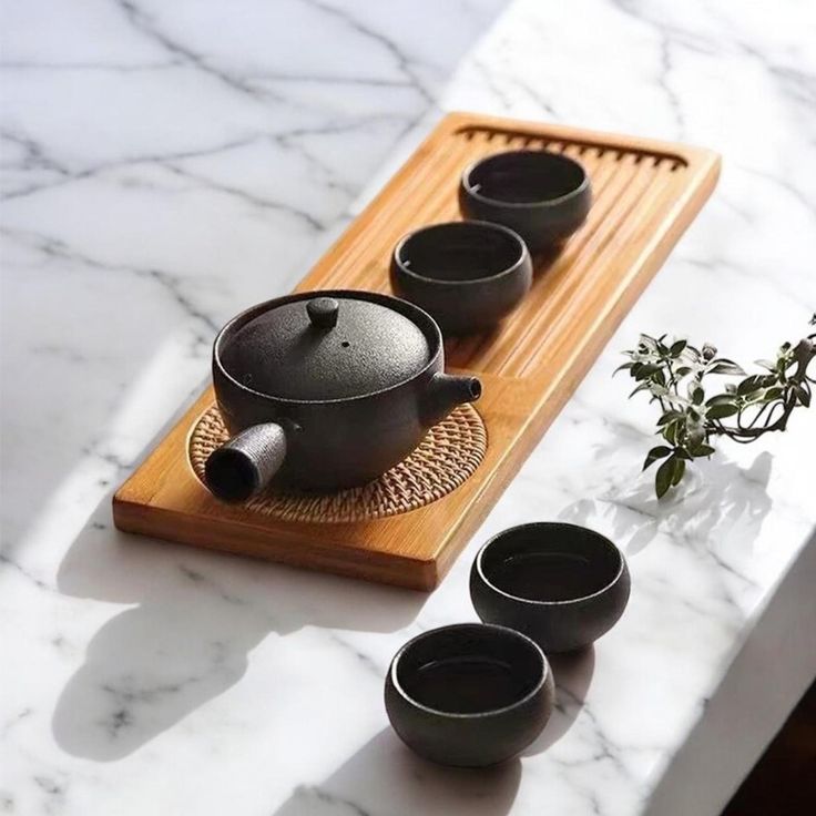 a tea set sitting on top of a wooden tray next to cups and a plant