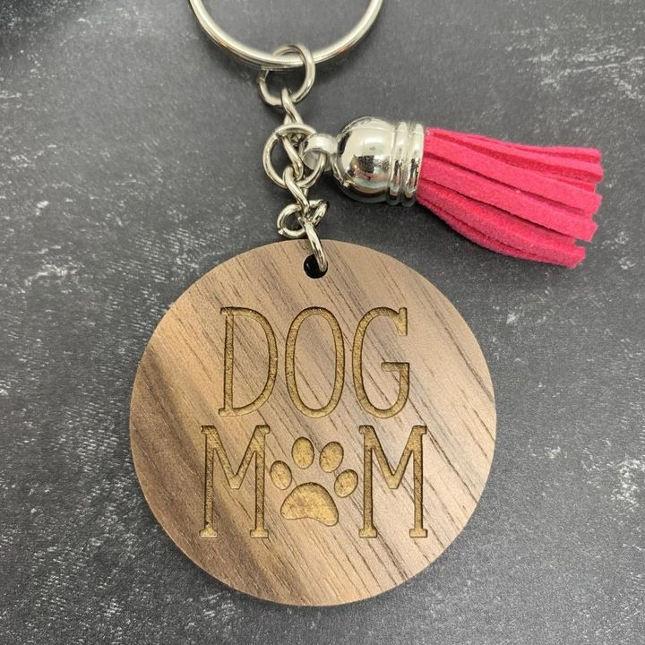 a wooden keychain that says dog mom with a pink tassel on it