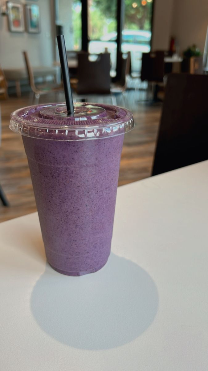 a purple drink sitting on top of a table next to a glass with a straw in it