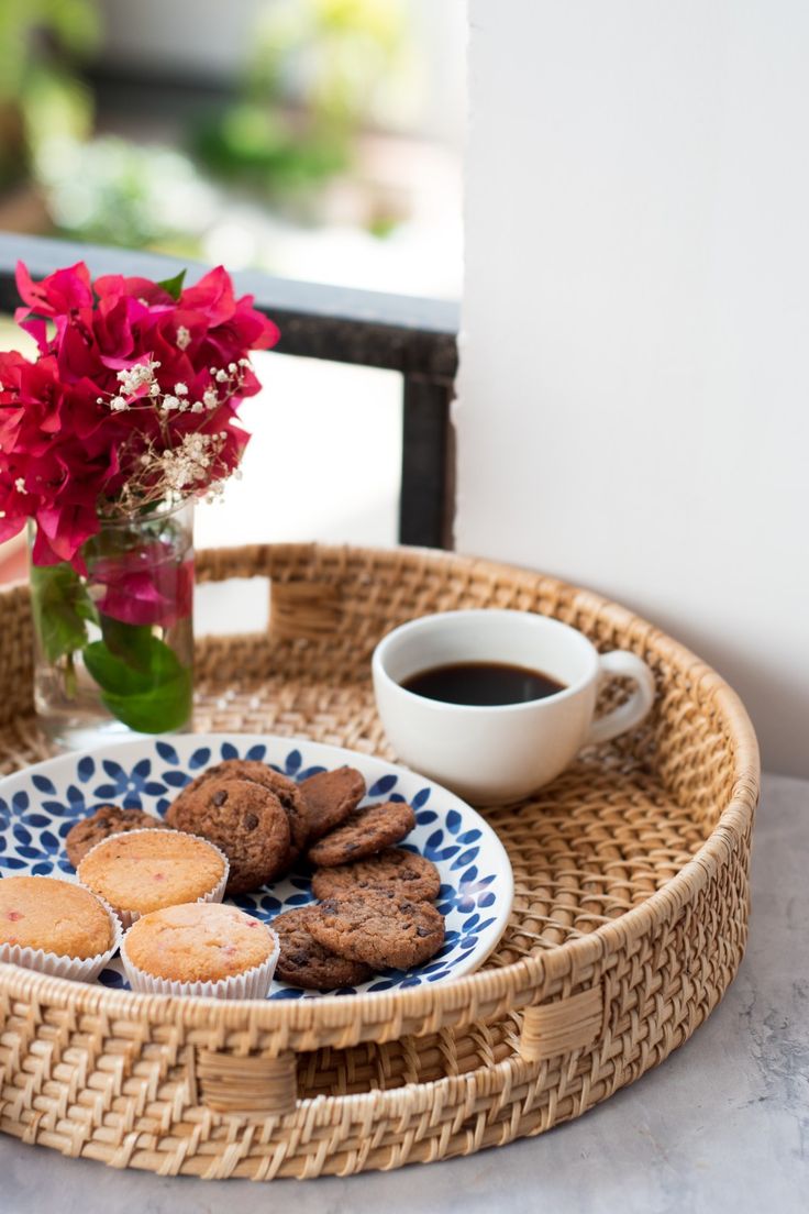 a wicker tray with cookies, coffee and flowers on it next to a window