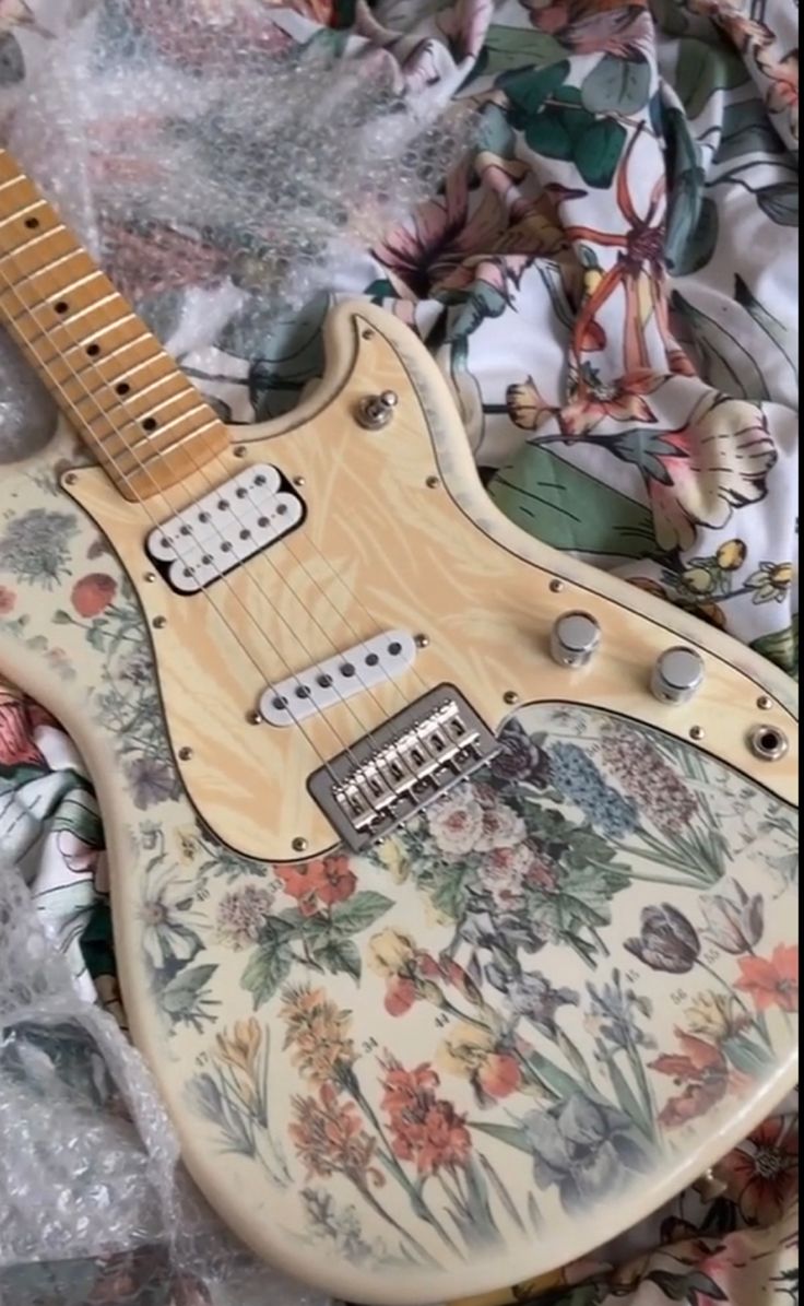 an electric guitar sitting on top of a bed covered in floral fabric and plastic wrap