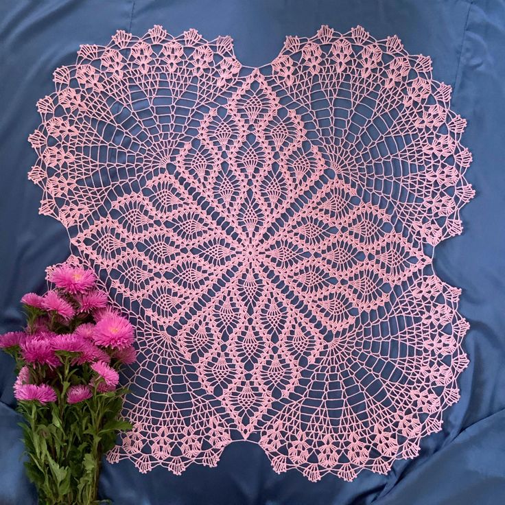 pink crocheted doily next to purple flowers on blue satin sheet with white background