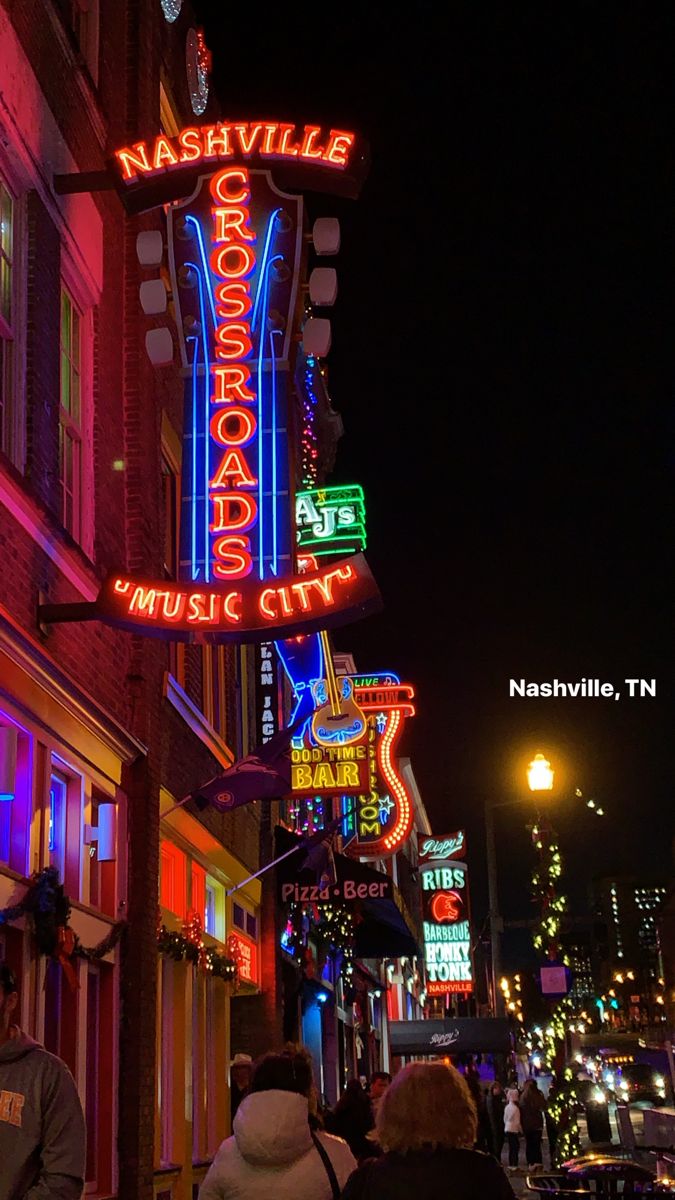 people walking down the street at night with neon signs on buildings in the city center