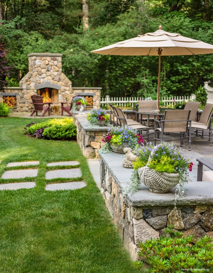 an outdoor patio with tables, chairs and umbrellas in the grass next to a stone fire place