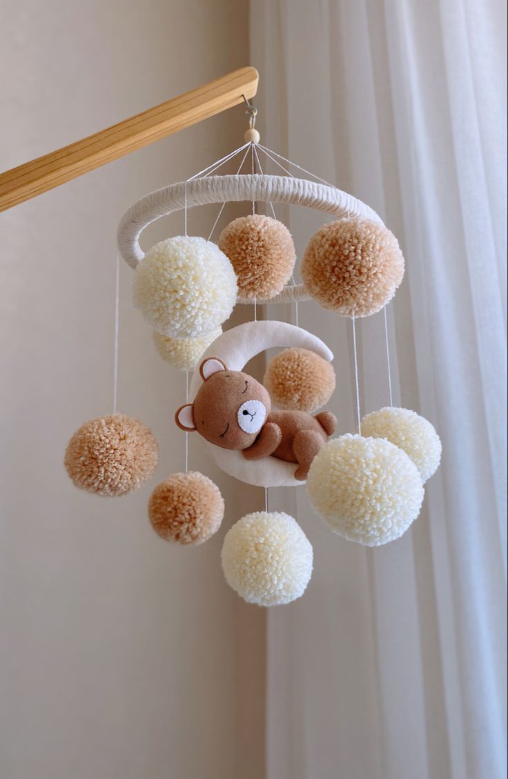 a teddy bear hanging from a white and beige mobile with pom - poms