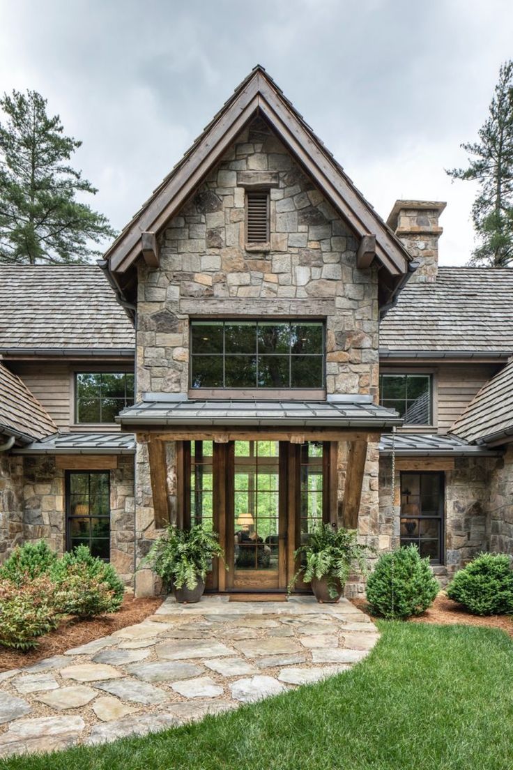 a stone house with large windows and lots of greenery on the front lawn area