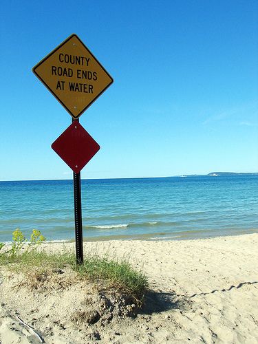 a road sign on the beach warning people to stay at the water's edge