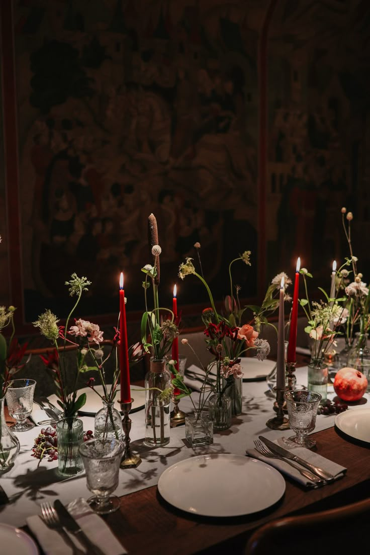 the table is set with candles and flowers in vases, plates and silverware