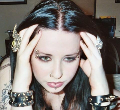 a woman with tattoos and piercings on her head holding her hands up to her face