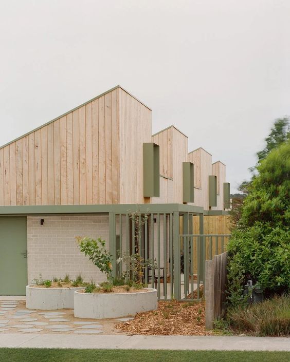 a building with wooden siding and green doors on the outside, surrounded by grass and trees