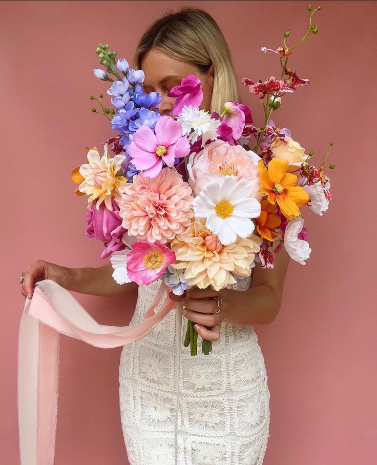 a woman in a white dress holding a bouquet of flowers and a pink ribbon around her neck