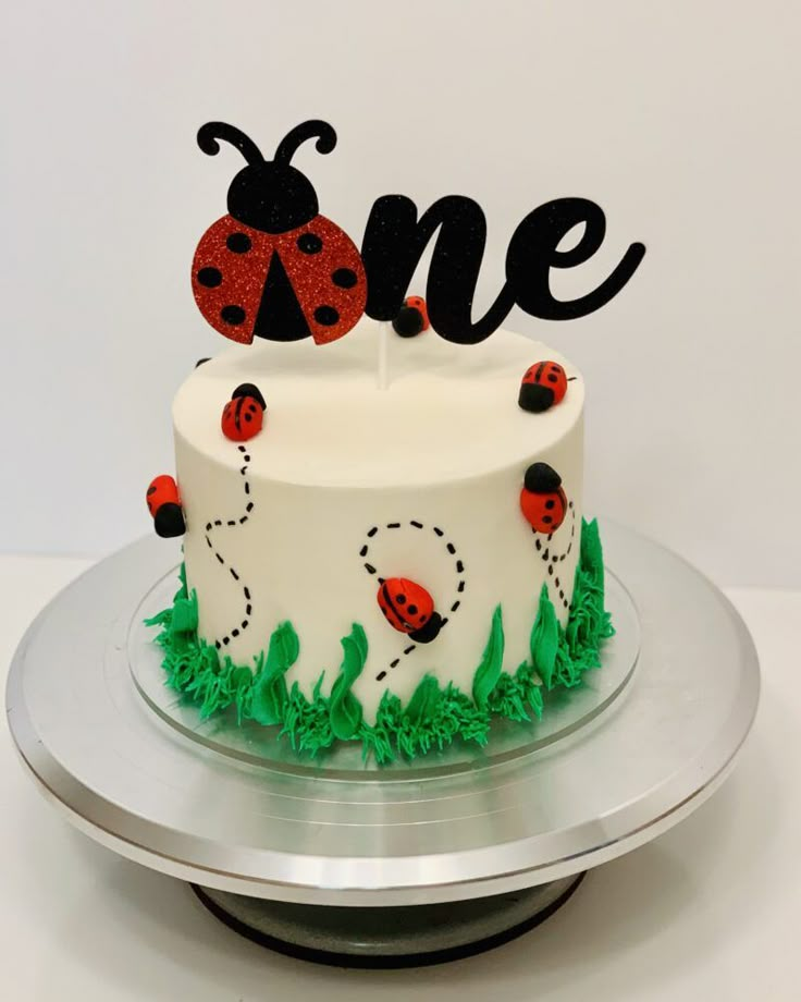 a birthday cake decorated with ladybugs and the word one on top is sitting on a silver platter