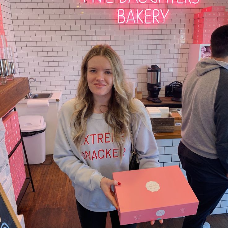 a woman holding a pink box in front of a counter