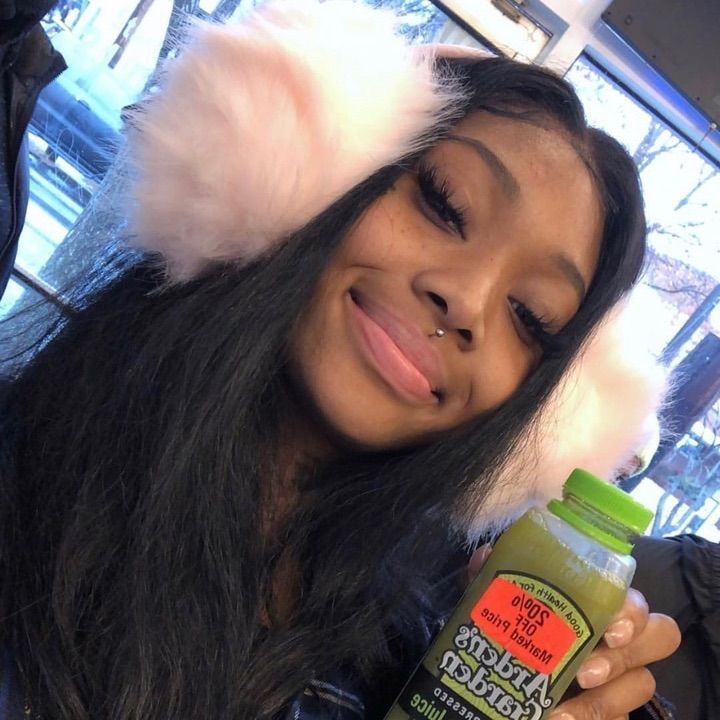 a woman holding a bottle of juice and wearing a furry hat on top of her head