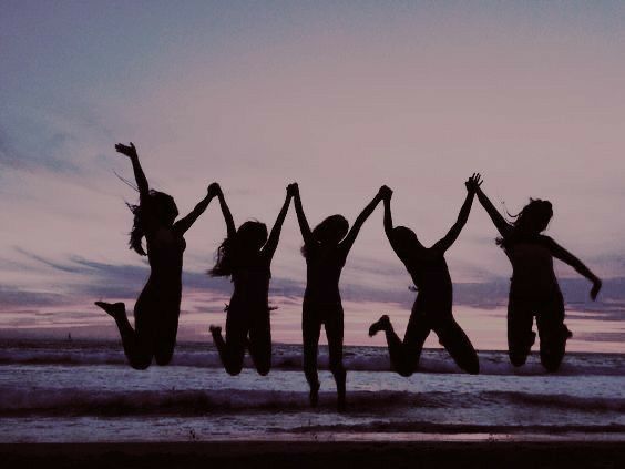 six people jumping in the air on a beach at sunset with their arms raised up