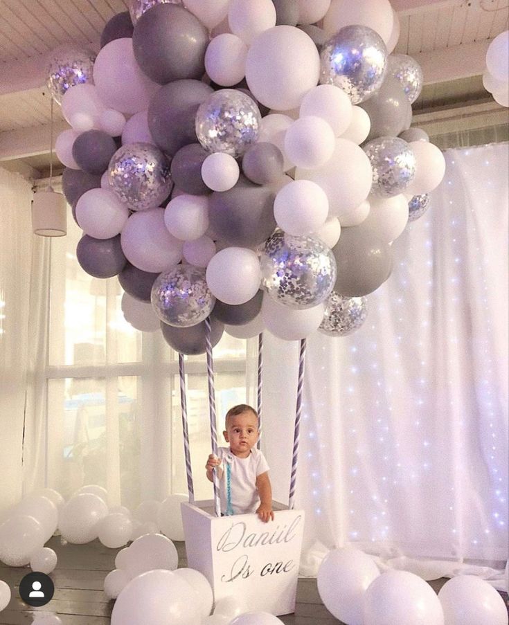 a baby in a box surrounded by white and silver balloons with the words diaper is one on it