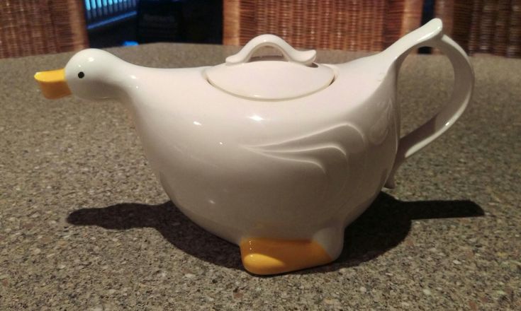 a white teapot with a yellow beak sitting on top of a counter