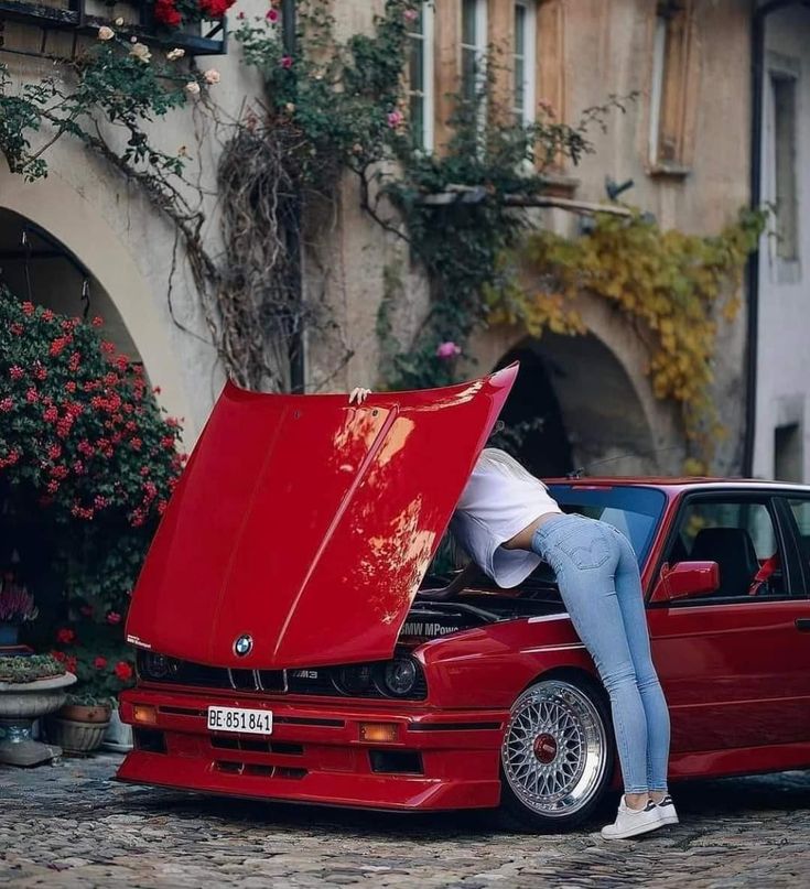 a woman leaning on the hood of a red car with it's hood open