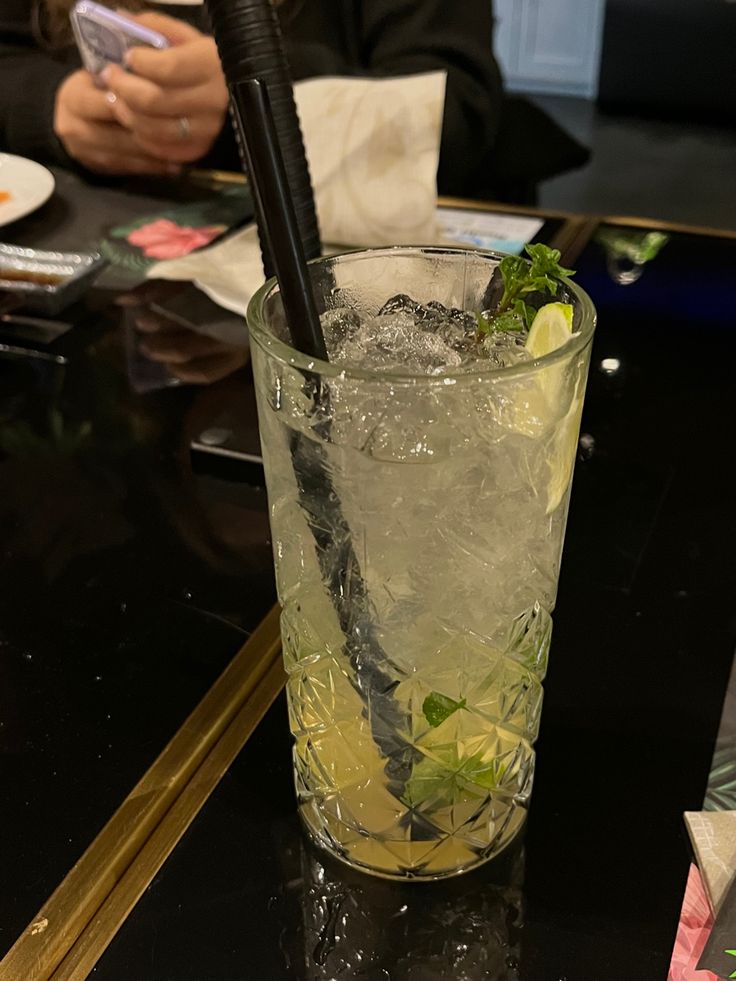 a glass filled with ice and limes sitting on top of a table next to a phone